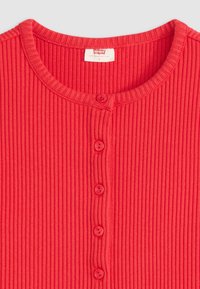 T-shirt rouge côtelé avec un col rond, six boutons assortis sur le devant et une étiquette avec les informations de marque et de taille.