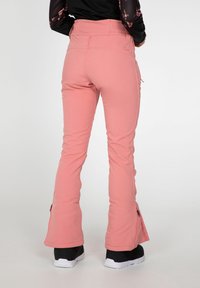 Pantalon de ski rose en tissu extensible, avec un bas évasé, des accents zippés près de l'ourlet et une taille ajustée.