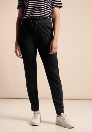 Pantalons noirs à coupe décontractée avec coutures à l'avant, taille élastique et cordon de serrage, associés à un haut à rayures à manches courtes et des sneakers blanches.