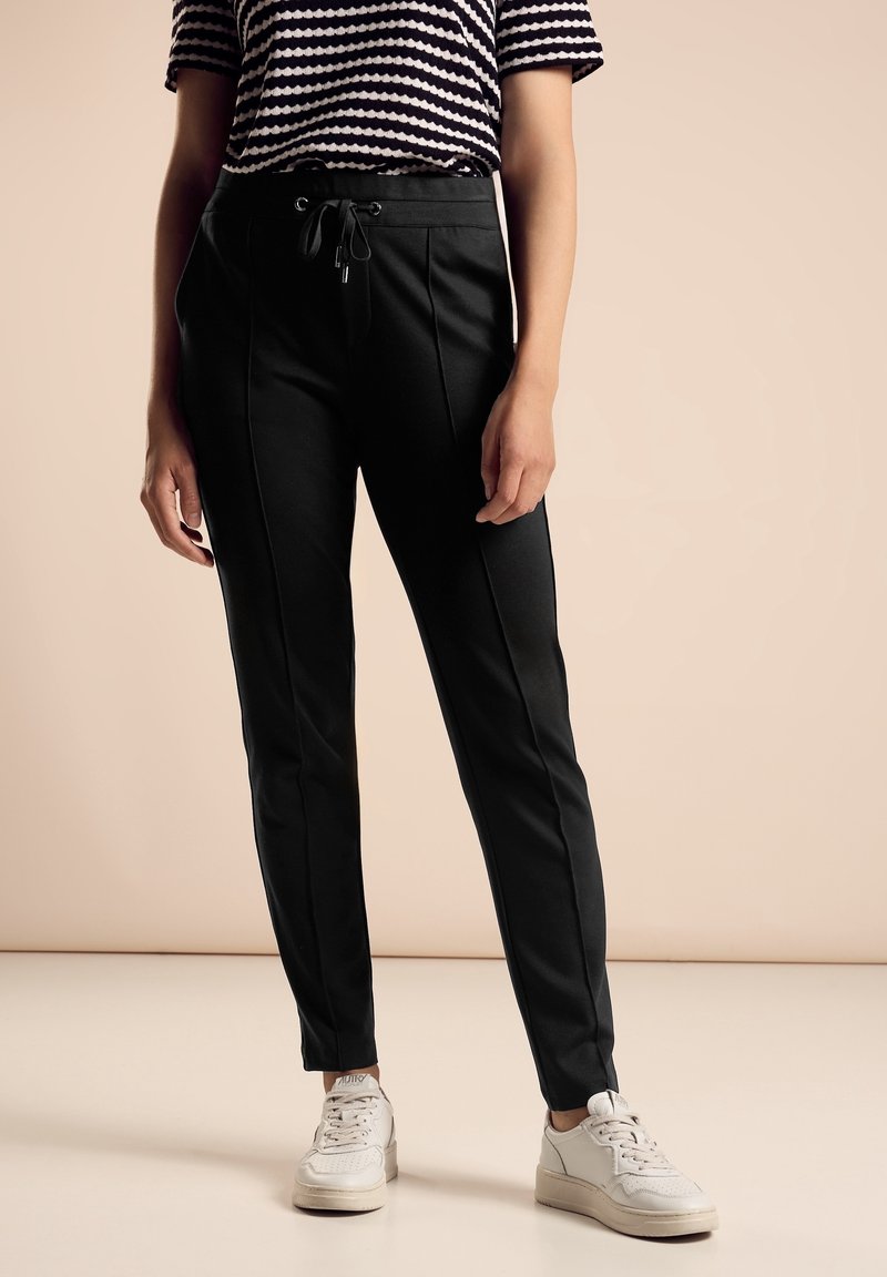 Svarta avslappnade byxor med framseams, elastisk midja och dragsko, kombinerat med en randig kortärmad topp och vita sneakers.