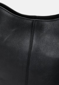 Borsa in pelle nera con una superficie liscia e cuciture visibili. Bordo superiore arrotondato e una texture delicata, che sottolineano la robustezza e lo stile.