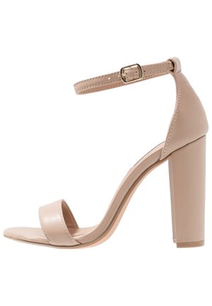 Sandal à talons hauts nude avec lanières, un épais talon bloc, en matériau synthétique lisse, une bride de cheville et une bande unique pour les orteils.