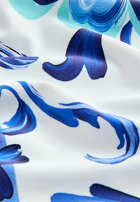 Textile à base blanche, présentant des motifs floraux abstraits en bleu et turquoise. Texture lisse avec des éléments de design en coups de pinceau fluides.