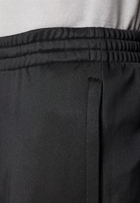 Črne športne hlače z elastičnim pasom, gladko teksturo in stranskimi žepi. Tkanina se zdi lahka in fleksibilna.