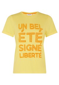 Žluté bavlněné tričko s krátkými rukávy se silným oranžovým textem: "UN BEL ÉTÉ SIGNÉ LIBERTÉ" v různých stylech písma. Jednoduchý design.