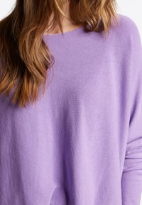 Fioletowy dzianinowy sweter o luźnym kroju, okrągłym dekolcie i miękkiej teksturze. Materiał wydaje się lekki i lekko przezroczysty.