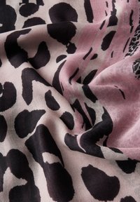 Luipaardprint sjaal van zachte stof, met grote zwarte vlekken op een roze achtergrond, met subtiele textuur en drapeerdetails.