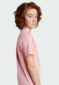 T-shirt en coton rose clair à manches courtes, doté d'un col rond et d'une coupe décontractée, présenté sur un fond neutre.