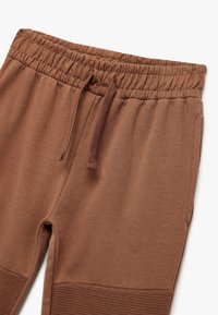 Brune sweatpants lavet af blødt stof, med elastisk taljebånd og snor, ribbede detaljer ved anklerne og glat tekstur.