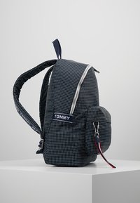 Mörkblå ryggsäck med rutmönster, utrustad med dragkedjestängning, frontficka och justerbara remmar. Finesser inkluderar en logotypetikett och en röd dragkedjeknop.