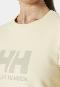 Sudadera amarilla claro con cuello redondo, que presenta un gran y sutil logo gris "HH" y la palabra "HENSON" en una fuente sencilla. Textura suave.