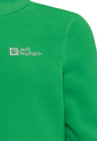 Giacca in fleece verde con colletto alto, caratterizzata da un logo ricamato in argento "Jack Wolfskin" sul petto e una texture morbida.