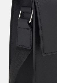 Borsa in tessuto nero con texture, dotata di una fibbia metallica argento e attacco per la tracolla. Presenta un flap liscio e dettagli con cuciture rinforzate.