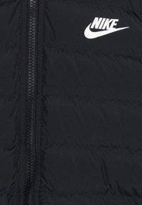 Svart puffjacka med dragkedja fram. Har sydda sektioner och en vit Nike-logga på övre vänstra delen. Slät, isolerad textur.