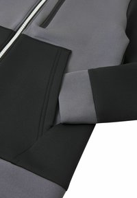 Giacca zip-up grigia e nera con una texture liscia, caratterizzata da una zip prominente, tasche nascoste e design delle maniche a contrasto.