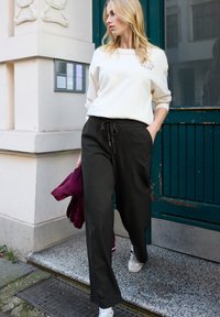 Kremowa bluza, czarne spodnie ze ściągaczem i białe trampki; gładkie kolory, luźny krój, zamek błyskawiczny na bordowej kurtce.