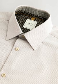 Helles Oberhemd mit strukturierten Streifen, Knopfkragen und kontrastierendem Innenstoff mit geometrischem Muster. Das Etikett trägt die Aufschrift "NEXT TAILORING".