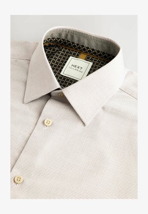 Helles Oberhemd mit strukturierten Streifen, Knopfkragen und kontrastierendem Innenstoff mit geometrischem Muster. Das Etikett trägt die Aufschrift "NEXT TAILORING".