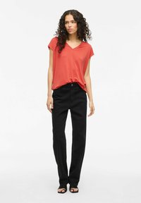 Top rojo de cuello en V, de manga corta, combinado con pantalones negros de pierna recta de cintura alta y sandalias negras. Tejido suave y corte relajado.