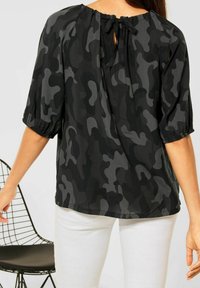 Blusa in tessuto leggero con stampa camouflage nera e grigia, maniche a sbuffo e scollatura con fiocco sul retro. Fit rilassato e orlo curvato.