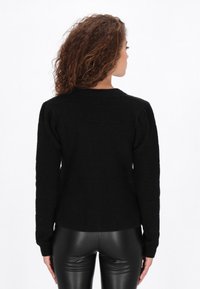 Czarny sweter dzianinowy o prążkowanej teksturze, z długimi rękawami i okrągłym dekoltem. Posiada dopasowany krój i lekko wzmocnione ramiona.