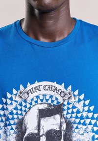Blå bomull t-shirt med rund hals, med en dödskalle grafik och texten "Just Cavalli" omgiven av spetsiga accenter i vitt.