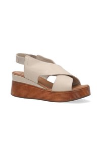 Beige kožené wedge sandály s otevřenou špičkou a kříženými popruhy. Obsahují šikmou dřevěnou platformu a elastický pásek na patě pro lepší přizpůsobení.