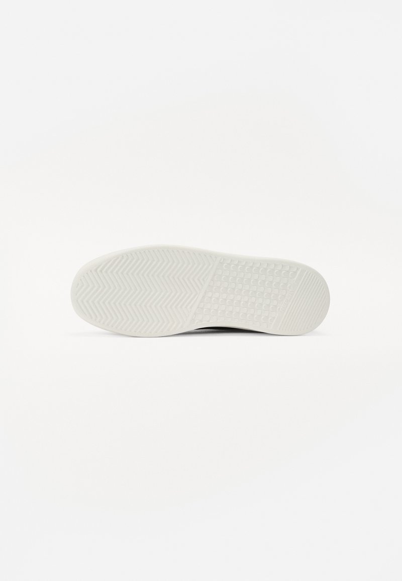 Semelle en caoutchouc blanche pour baskets, présentant un motif en chevrons texturé et une surface lisse avec des sections adhérentes pour une meilleure traction.