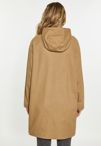 Cappotto beige con cappuccio e vestibilità rilassata, caratterizzato da un taglio dritto, maniche lunghe e dettagli sulle cuciture. Realizzato in un materiale liscio e leggero.