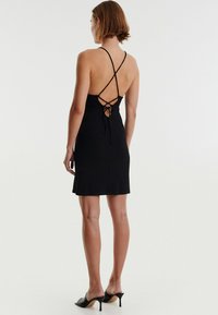 Zwarte ribbed jurk met een lage rug en crisscross bandjes, voorzien van een striksluiting. Glad materiaal, nauwsluitende pasvorm, lengte tot de knie.