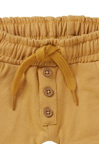 Senfgelbe Baumwollshorts mit einem gerafften elastischen Bund, ausgestattet mit einer geknoteten Kordel und drei Holzknöpfen.