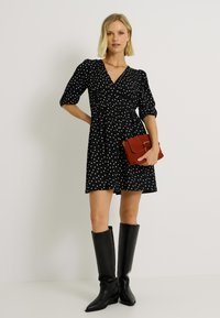 Vestido negro con lunares, con escote en V y mangas abullonadas, combinado con botas negras hasta la rodilla y un bolso de mano rojo.
