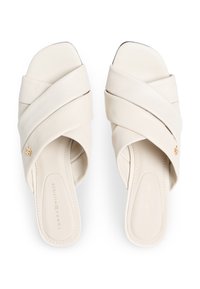 Σανδάλια τύπου σλάιντ σε κρεμ απόχρωση με διασταυρωμένους δερμάτινους ιμάντες, ομαλή υφή και μικρό χρυσό λογότυπο κοντά στην πλευρά.