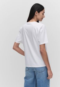 Biała koszulka z krótkim rękawem, wykonana z bawełny, z okrągłym dekoltem i luźnym krojem, zestawiona z jasnoniebieskimi dżinsami o wysokim stanie.