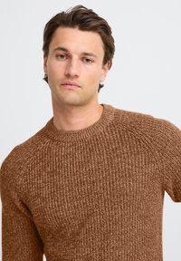 Brun strukturstrikket sweater med rund hals og raglanærmer. Let varieret stingmønster over det hele.