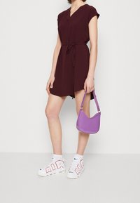 Burgundy kortärmad klänning med knytliv, tillsammans med en glänsande lila handväska och vita sneakers med röda bokstäver och blå accentfärger.