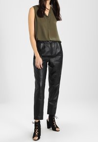 Blouse sans manches vert olive, pantalons en cuir noirs taille haute, et sandales à lacets noires à talon épais.