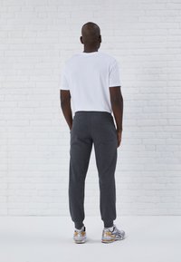 Camiseta blanca de manga corta, pantalones de chándal grises con cintura elástica y bolsillo trasero, combinados con zapatillas de running multicolor sobre una superficie texturizada.