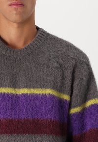 Maglione grigio a maglia con una texture morbida, caratterizzato da strisce orizzontali gialle, viola e bordeaux sulla parte anteriore. Collo rotondo.