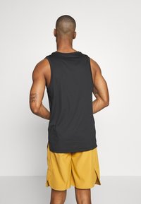 Débardeur noir sans manches à coupe décontractée, associé à un short jaune. Le haut présente un col arrondi et des fentes latérales.