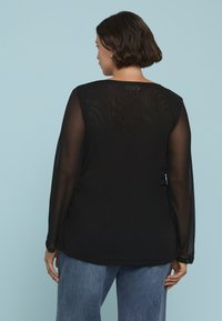 Schwarzes Langarmshirt mit durchsichtigen Ärmeln, glatter Textur und entspanntem Schnitt, kombiniert mit hellblauen, hoch taillierten Jeans.