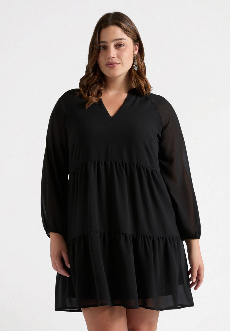 Vestido negro con escote en V, mangas largas y transparentes, y diseño en capas. Presenta una tela ligera y fluida con una textura sutil.