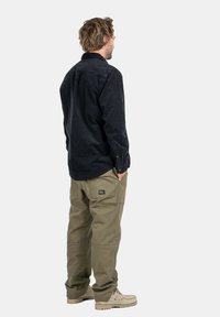 Camicia in velluto a coste nera con polsini abbottonati abbinata a pantaloni cargo verde oliva dotati di tasche e un'etichetta. Calzature beige completano l'outfit.
