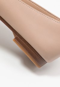 Chaussure slip-on synthétique beige avec un intérieur texturé et une semelle marron clair, présentant un dessus lisse et un subtil détail de coutures.