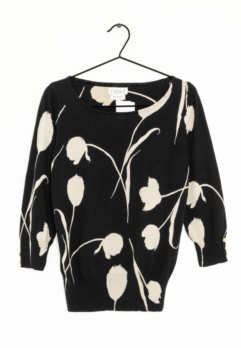 Pull noir à manches longues avec motif floral abstrait blanc, col rond et trois petits boutons sur chaque manchette, suspendu à un cintre noir.