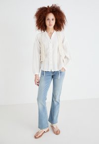 White, button-up blouse with textured fabric and balloon sleeves, paired with light blue flared jeans. Strappy sandals complete the look.