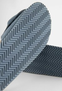 Grå gummisål med et zigzag-mønster, der har en overdel i suede i lignende farve. Designet er enkelt og fladt.