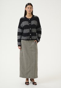 Striped cardigan in navy and gray knit with round buttons, paired with a long, textured skirt in herringbone pattern and open-toe heels.