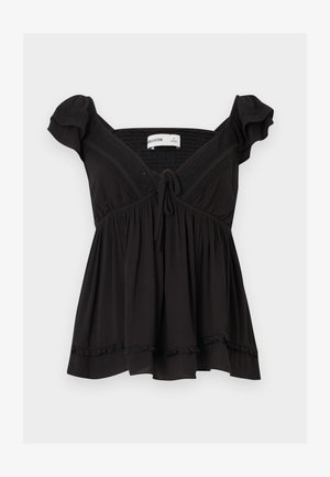 Melns plecu atsegts tops ar īsām volānveida piedurknēm, priekšā aizdares lentu, teksturētu audumu un savilktu vidukļa līniju ar volāniem apakšmalā.