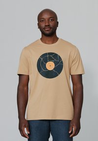 Beige t-shirt met een centraal grafisch ontwerp van een gebroken vinylplaat in donkerblauw met een oranje label, gemaakt van zachte katoen.